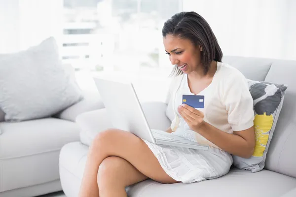 Delighted young woman in white clothes shopping online with a laptop