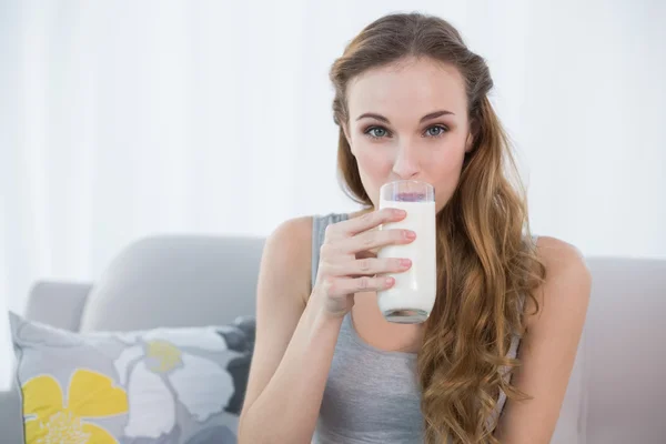 Happy young woman sitting on sofa drinking milk