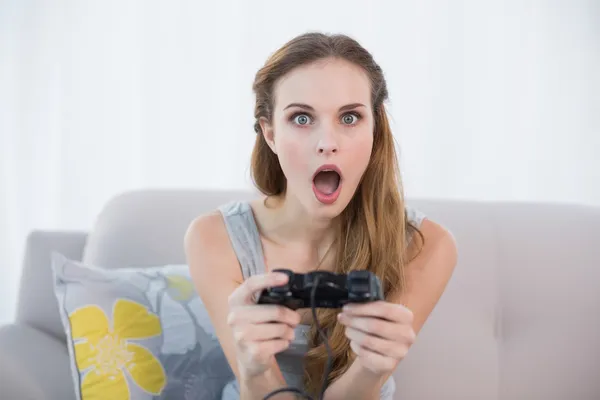 Shocked young woman sitting on sofa playing video games