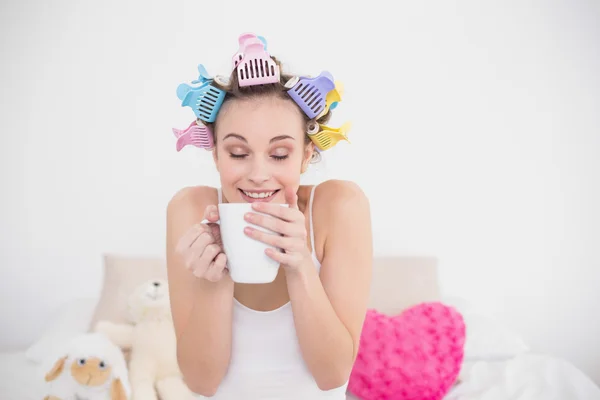 Funny woman in hair curlers enjoying coffee smell