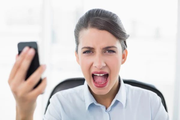 Annoyed businesswoman screaming while holding a mobile phone