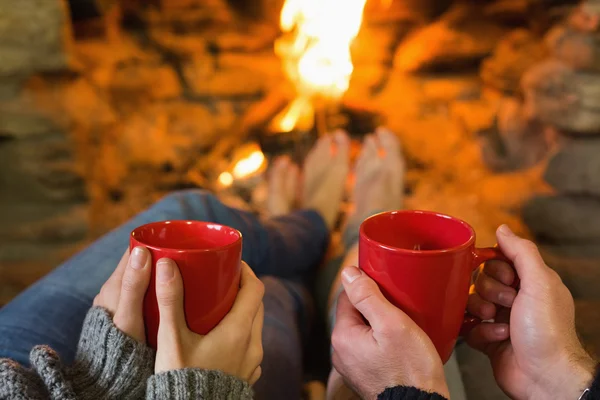 Hands with red coffee cups in front of lit fireplace