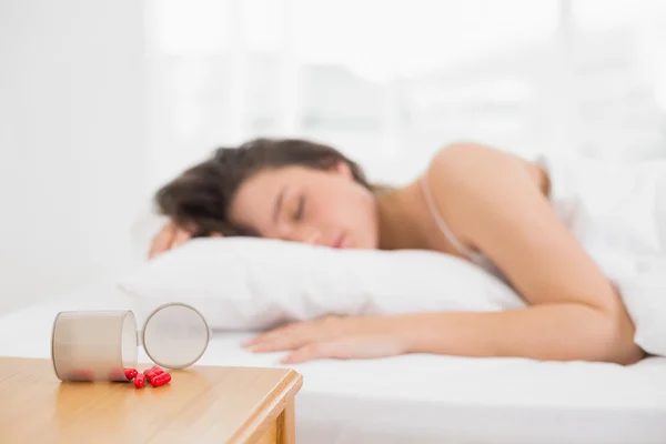 Blurred woman sleeping in bed with pills in foreground