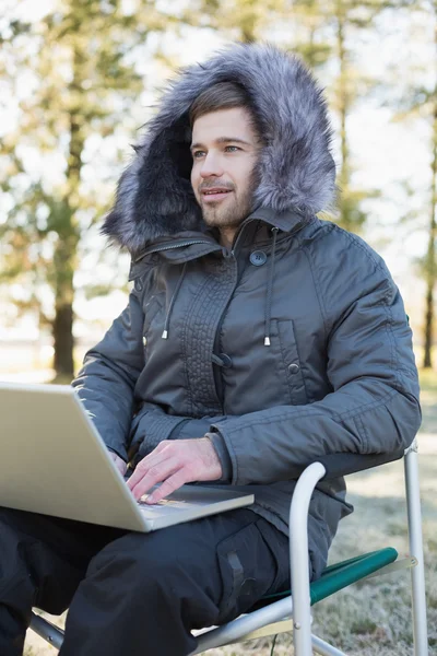 Young man in fur hood jacket using laptop in the forest
