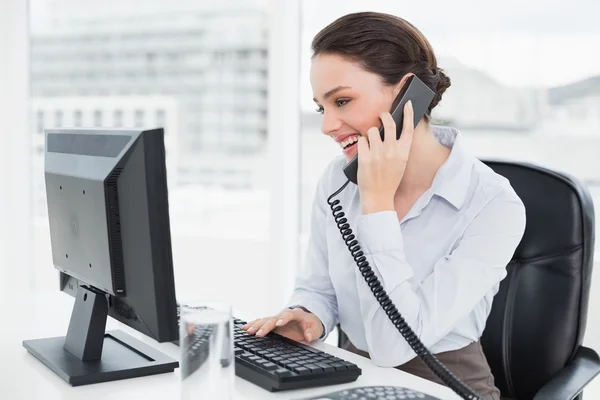Elegant businesswoman using landline phone and computer in office