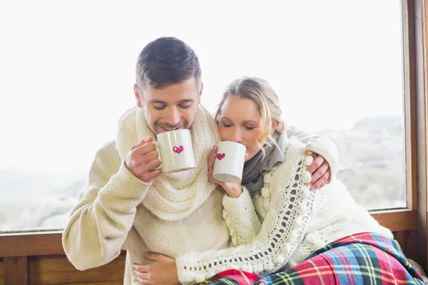 Loving couple in winter wear drinking coffee against window