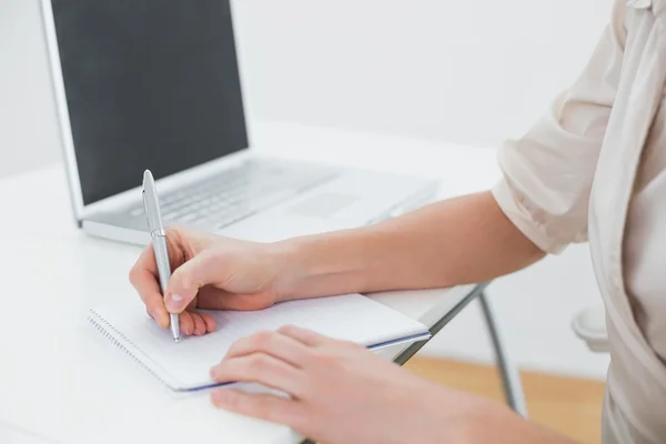 Midsection of a businesswoman writing notes by laptop