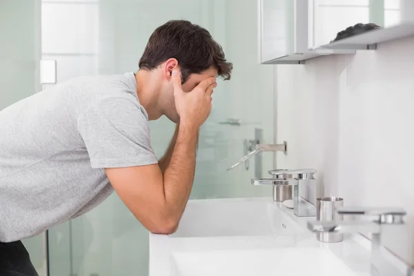 Young man with head in hands at washbasin