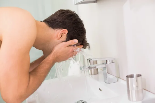 Shirtless young man washing face in bathroom