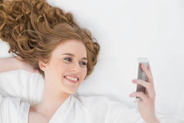 Relaxed blond looking at mobile phone in bed