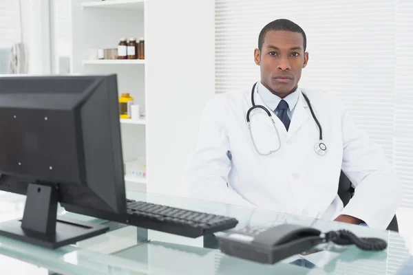 Serious male doctor sitting with computer at medical office