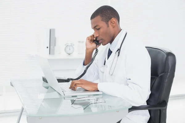 Male doctor using phone and laptop at medical office