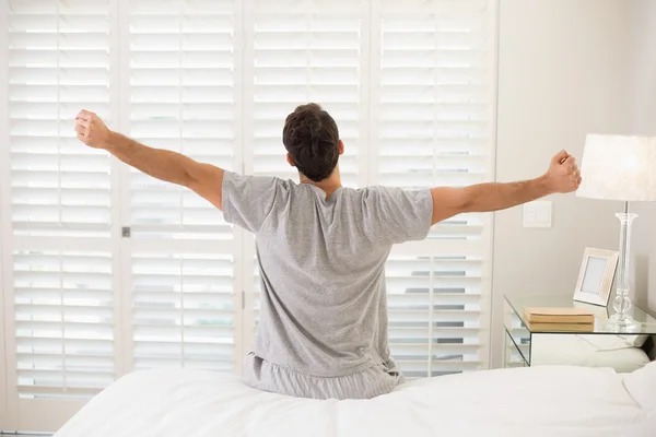 Rear view of man stretching his arms in bed
