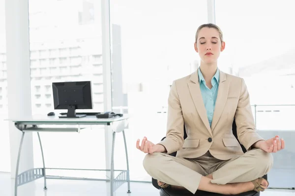 Lovely classy businesswoman meditating in lotus position on her swivel chair