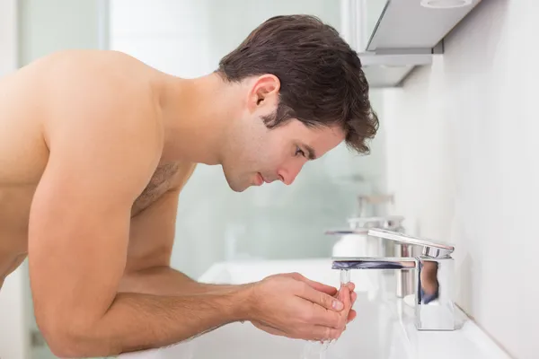 Side view of shirtless man washing face in bathroom