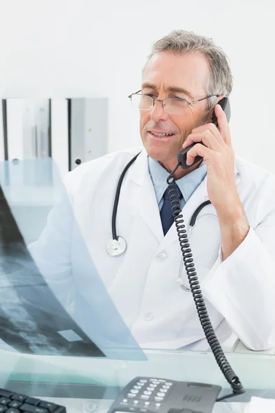 Doctor with x-ray picture using telephone at office