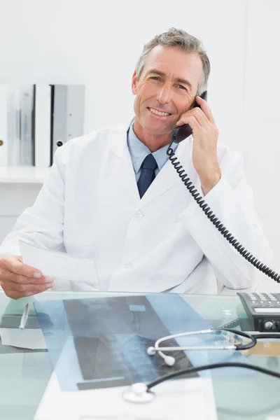 Doctor using telephone while looking at note in office