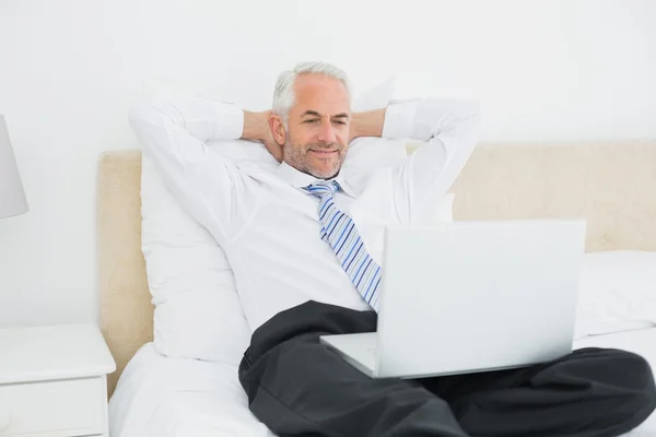 Relaxed businessman looking at laptop in bed
