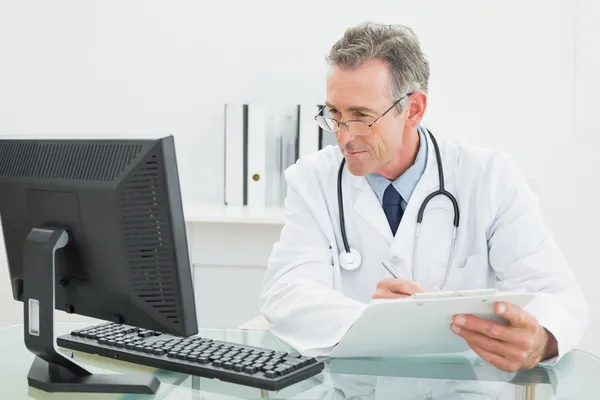 Doctor with report looking at computer monitor at medical office