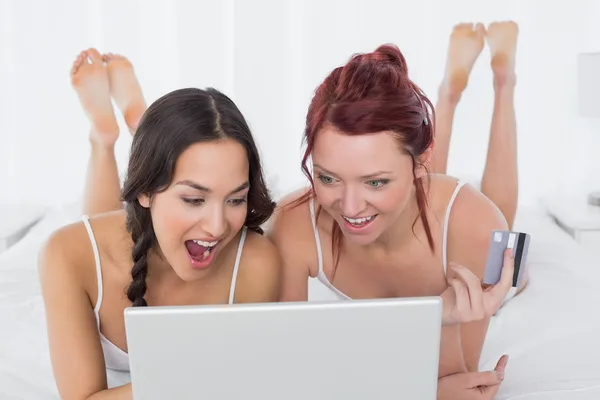 Cheerful female friends doing online shopping in bed
