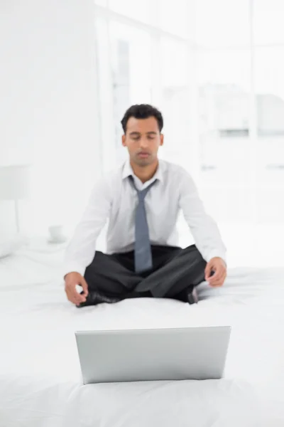 Businessman sitting in lotus pose with laptop on bed