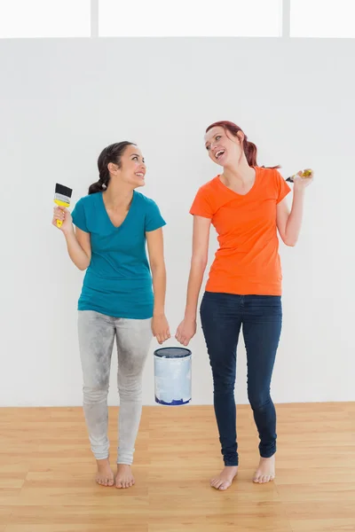 Cheerful friends with brushes and paint can in new house