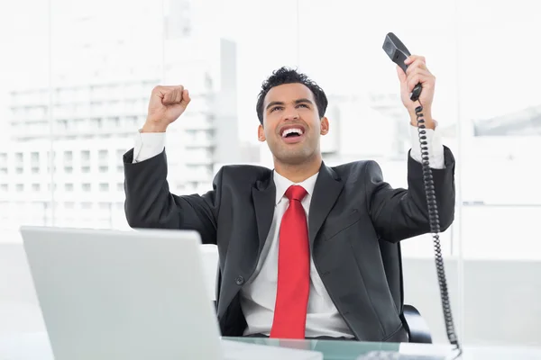 Businessman cheering with telephone receiver at office