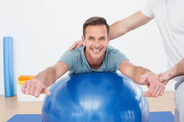 Physical therapist assisting young man with yoga ball