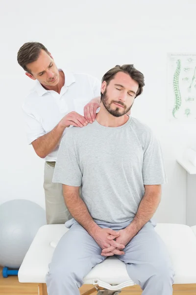 Male therapist massaging a content man\'s shoulders