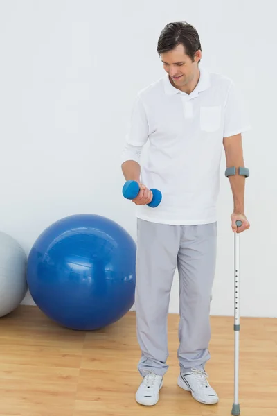 Smiling young man with crutch and dumbbell
