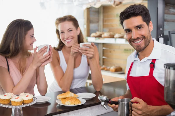Women drinking coffee with male barista at coffee shop counter