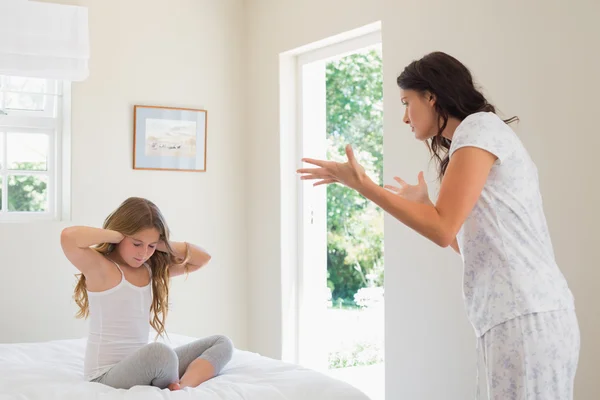 Girl covering ears while mother scolding bedroom