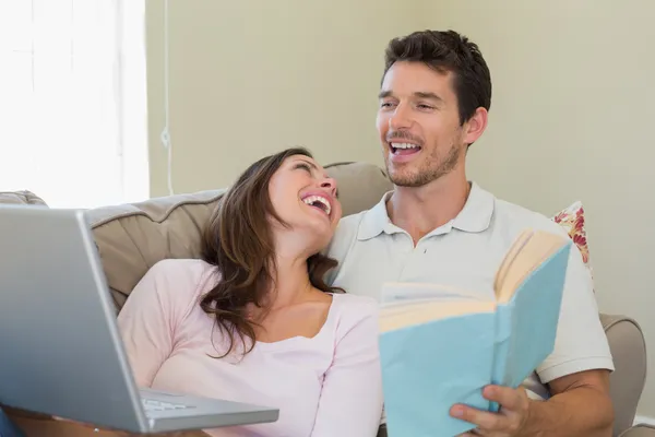 Cheerful couple with laptop and book at home