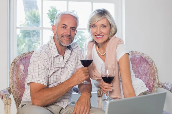 Relaxed mature couple with wine glass using laptop