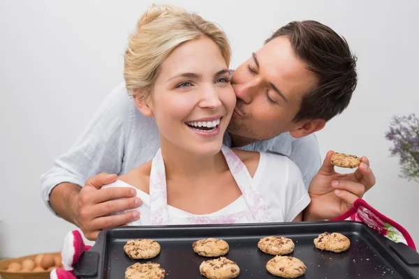 Man kissing woman's cheek as she holds freshly baked cookies in