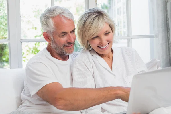 Happy mature couple using laptop in bed