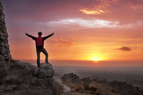 Man on top of a mountain victorious admiring the sunrise