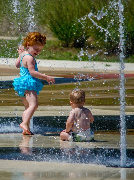 Toddler and baby brother play in summer fountain