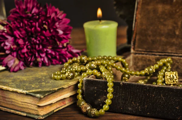 Old book, flower, candle and open jewelry box with green necklace still life, renaissance concept with dark grunge light