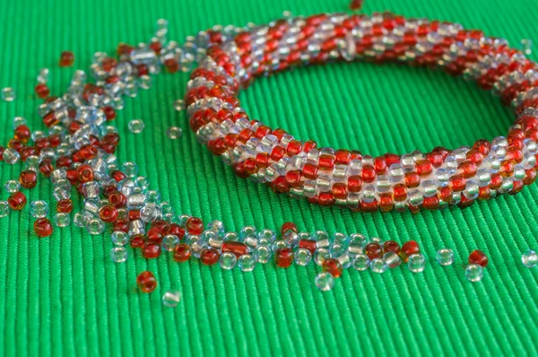 Knitted bracelet from red and gray beads on a green background