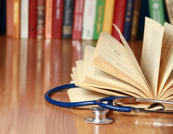 A stethoscope is lying with a book on the desk against books.