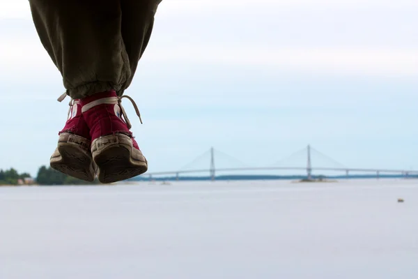 Girls legs with red used converse shoes hanging down and bridge on horizon