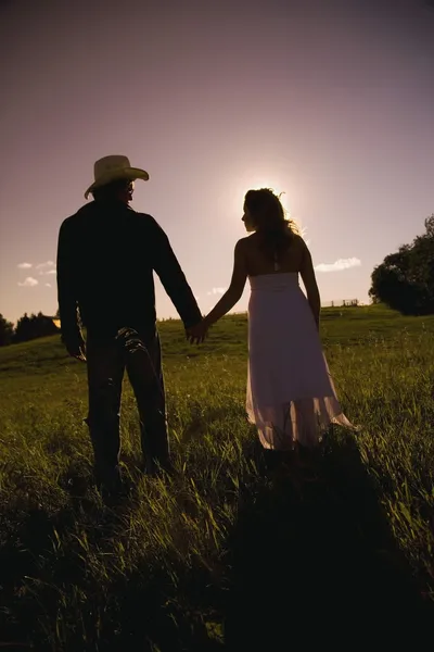 Man And Woman Walking Hand-In-Hand In Field In Sunset