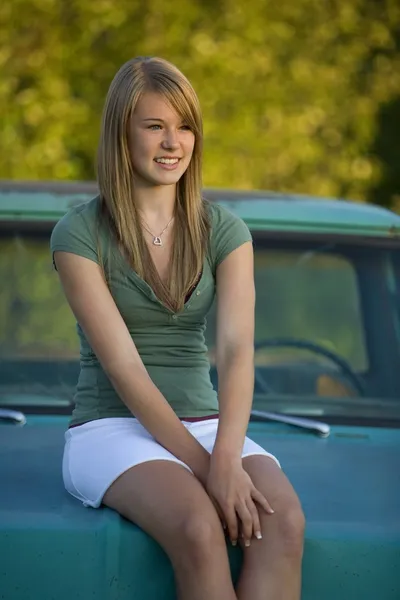 Young Woman Sits On Hood Of Old Truck