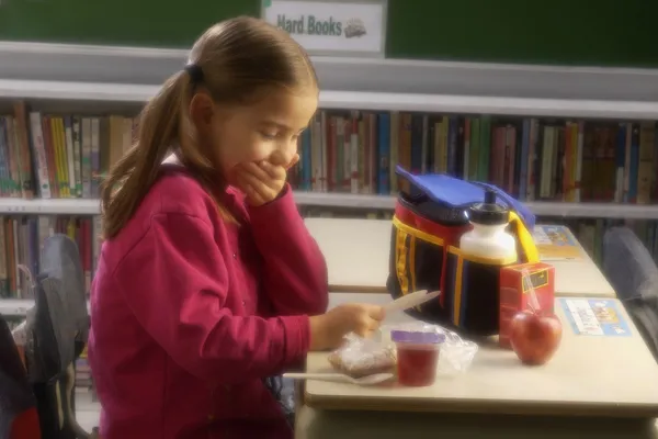 Girl Eating Lunch At Desk Reading A Card
