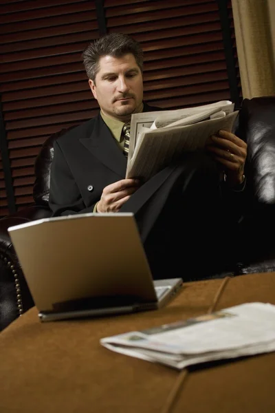 Businessman Reading The Newspaper With His Laptop