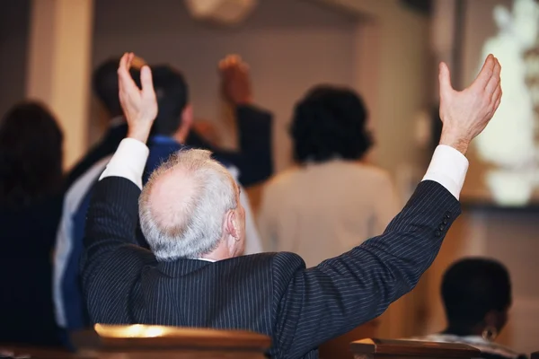 Man Sitting In Church With Hands Raised