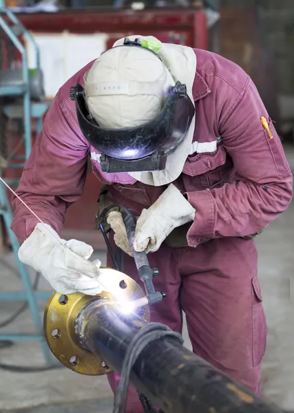 Craftman in a safety suit is welding a metal pipe