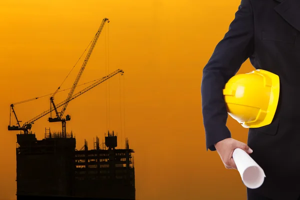 Engineer holding yellow helmet for workers security on background of new highrise apartment buildings and construction cranes