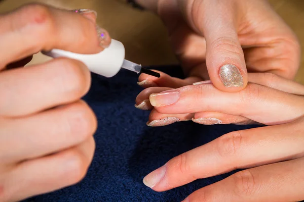 Beautician applying nail varnish to the fingernails of a client